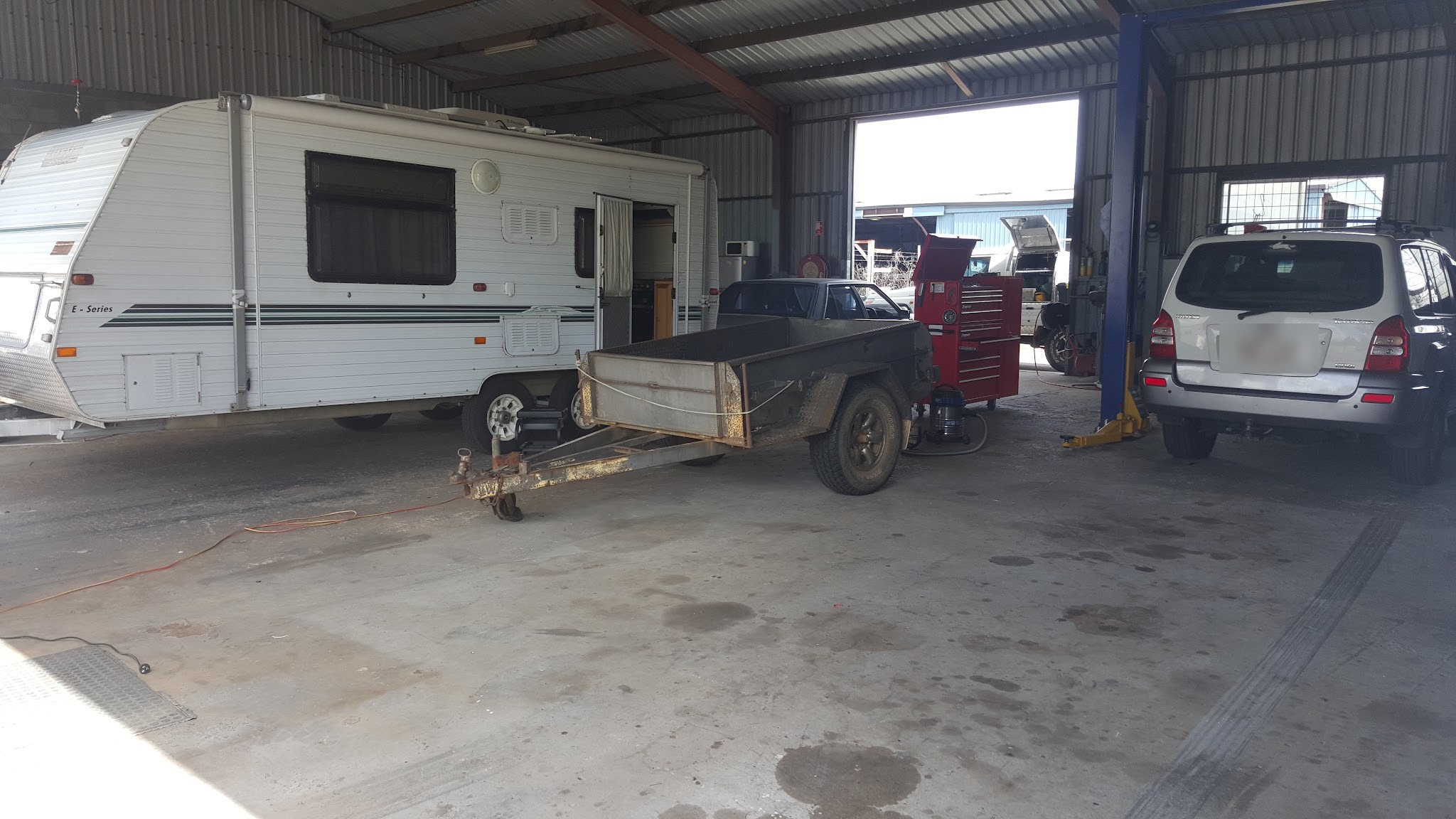 A caravan and a trailer in the workshop alongside a vehicle on the hoist